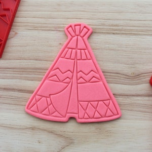 May include: Pink plastic cookie cutter shaped like a teepee with geometric patterns.