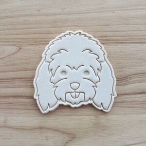 Op de afbeelding: Witte plastic koekjesvormer in de vorm van een hondenkop met pluizig haar.
