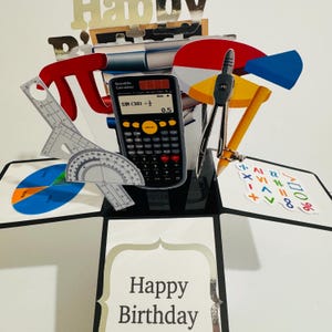 Könnte beinhalten: Eine dreidimensionale Pop-up-Grußkarte mit einem wissenschaftlichen Taschenrechner, der SIN(30)=0,5 anzeigt, einem Metallzirkel, einem Winkelmesser, einem Lineal und bunten Tortendiagrammen. Die Karte enthält den Text Happy Birthday.