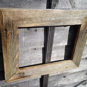 May include: A rustic wooden picture frame with a weathered, natural finish. The frame is made of reclaimed wood and has a rectangular shape.