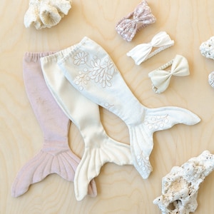 Peut inclure: Deux costumes de queue de sirène, l'un de couleur rose clair et l'autre de couleur crème avec un motif floral. Les queues sont en tissu doux et ont un bord festonné. Il y a aussi trois accessoires pour cheveux, deux nœuds et un bandeau, de couleur rose clair.