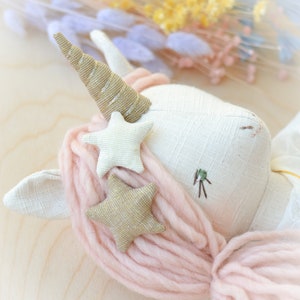 May include: A white unicorn doll with a gold horn and pink yarn hair. The doll has two gold glitter stars and one white star sewn on its head.