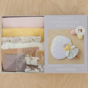 Könnte beinhalten: Ein Nähset zum Nähen einer kleinen Puppe. Das Set enthält Stoffreste, Füllmaterial und Garn. Die Schachtel ist mit "Kit de Couture Sewing Kit" und "Mini Robine" beschriftet.