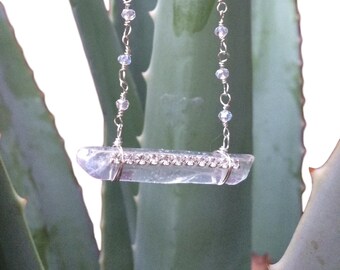 May include: A clear crystal pendant necklace with a silver chain and rhinestones. The pendant is a long, thin piece of crystal with a row of rhinestones running down the center.
