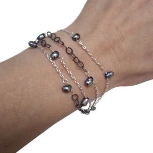 May include: A layered bracelet with a silver chain and a black chain. The bracelet is adorned with small, dark gray pearls.