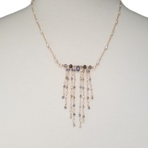 May include: A gold necklace with a delicate chain and a cascading fringe of small, faceted gemstones in shades of gray and purple.