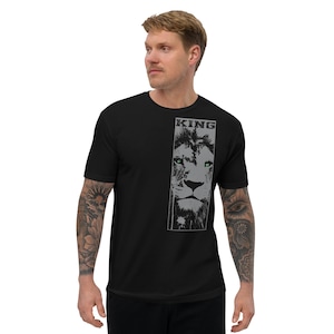Puede incluir: Camiseta negra con un diseño de león gris y la palabra "KING" encima. Los ojos del león son verdes. La camiseta está hecha de un material suave.