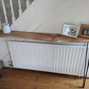 May include: A long, narrow wooden console table with a live edge top and black hairpin legs. The table is decorated with a white ceramic vase and two framed photos of dogs.