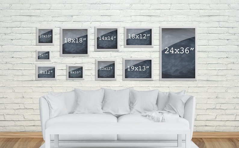 May include: A white brick wall with a white couch and nine white picture frames with black and white images and measurements in inches. The frames are arranged in a staggered pattern.