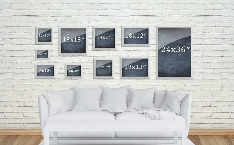 May include: A white brick wall with a white couch and 10 picture frames of various sizes. The frames are all white and have black numbers inside indicating the size of the frame in inches. The frames are arranged in a staggered pattern on the wall.