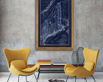May include: A framed vintage map of Maine with a blue background and white lines. The map is hanging on a gray wall with two yellow chairs and a coffee table in front of it.