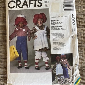 May include: McCall's Crafts sewing pattern 4097 for Raggedy Ann and Andy costumes in size 6/8. The envelope features illustrations of two children wearing red yarn wigs, blue and white checkered shirts, blue trousers, white aprons, and striped socks.