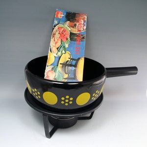 May include: A black fondue pot with yellow polka dots, a long handle, and a metal stand. A vintage "Fondue Fork Set" pamphlet is inside the pot. The pot sits on a metal stand with a fuel holder.