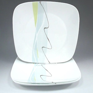 May include: A set of white square plates featuring a graphic design of vertical light blue and lime green bands accented by a thin, wavy dark gray line. The plates have rounded corners and a smooth, glossy finish on the surface.