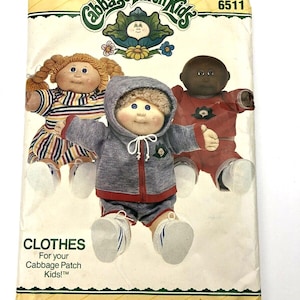 May include: Vintage Butterick sewing pattern for Cabbage Patch Kids clothes. The pattern features illustrations of three Cabbage Patch Kids dolls wearing different outfits. The pattern envelope is cream-colored with green and yellow accents and the text "CLOTHES" and "BUTTERICK".