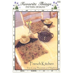 May include: A catalog cover featuring a tea set and accessories. The image includes a teapot cozy, placemats, and napkins with a floral pattern. The text reads "French Kitchen" and "Tea Cozy, Placemats and Napkins."