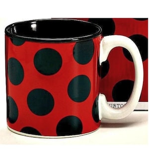 May include: A ceramic mug with a red background and large black polka dots. The interior of the mug is black, and the handle is white. The mug is a fun and whimsical design.