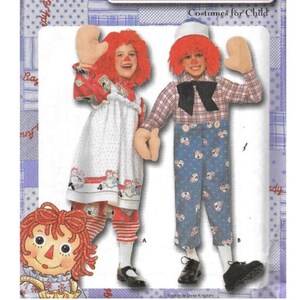 May include: Costumes for Child. Two children dressed in Raggedy Ann and Andy costumes. The Raggedy Ann costume includes a white dress with red trim and a red wig. The Andy costume features a plaid shirt and blue pants. Both costumes have large beige mittens.