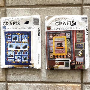 May include: Two McCall's Crafts sewing pattern envelopes. The left envelope, number 2443, shows a blue winter-themed quilt with snowmen and trees. The right envelope, number 3277, displays a quilt featuring sewing motifs and a sewing machine.