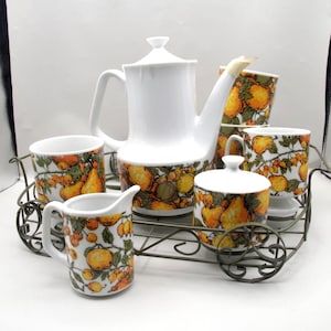 May include: A white porcelain coffee set with a fruit pattern, including a coffee pot, creamer, sugar bowl, and cups, presented on a decorative metal cart. The fruit design features oranges, pears, and green leaves. The set is ideal for serving coffee or tea.
