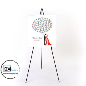 May include: A white wedding guest book with a black easel stand. The book features a fingerprint tree design with a couple in silhouette. The text reads "Thao & Steven 08.20.2017".
