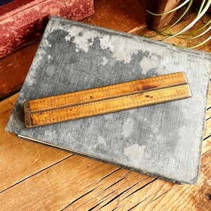 May include: A wooden folding ruler with brass accents and markings in inches. The ruler is closed and lying on a dark gray surface.