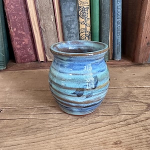 May include: A small, blue and brown ceramic vase with a rounded body and a wide opening. The vase has a striped pattern with shades of blue, brown, and white.