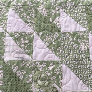 May include: A quilt made of green and white fabric with a floral pattern. The quilt is quilted with a swirl pattern.