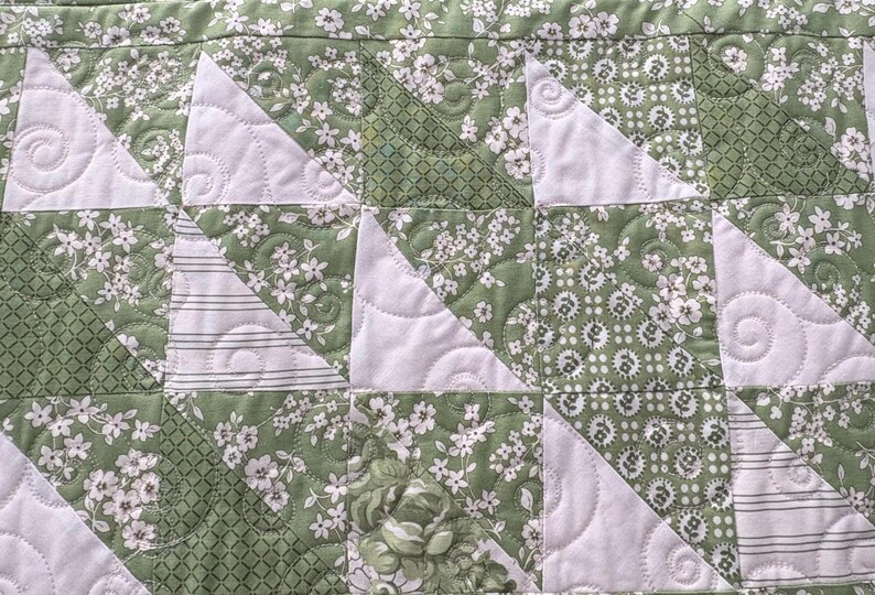 May include: A quilt made of green and white fabric with a floral pattern. The quilt is quilted with a swirl pattern.