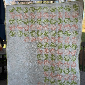 May include: A quilt featuring a patchwork of hexagonal fabric pieces in shades of sage green and soft peach, each printed with a floral pattern. The lower left section consists of solid cream fabric with intricate quilted floral stitching details.
