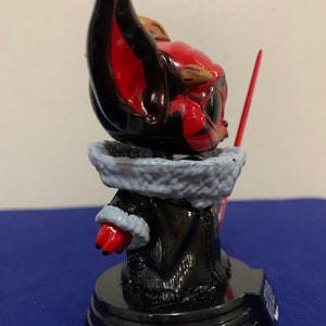 May include: A red and black painted figurine of a character from the Star Wars franchise. The character is wearing a black robe with a white fur collar and holding a red lightsaber. The figurine is standing on a black base.