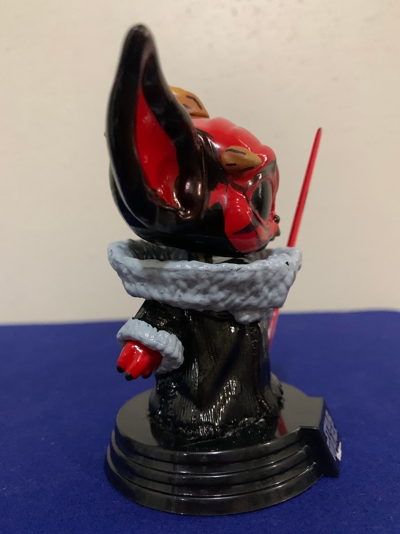 May include: A red and black painted figurine of a character from the Star Wars franchise. The character is wearing a black robe with a white fur collar and holding a red lightsaber. The figurine is standing on a black base.