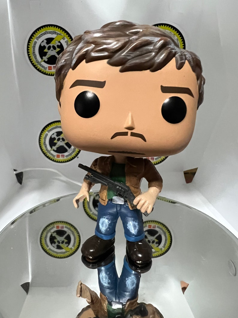 May include: A brown-haired pop culture figure with a moustache, wearing a brown jacket, blue jeans, and brown boots, holding a black shotgun. The figure is standing on a reflective surface.