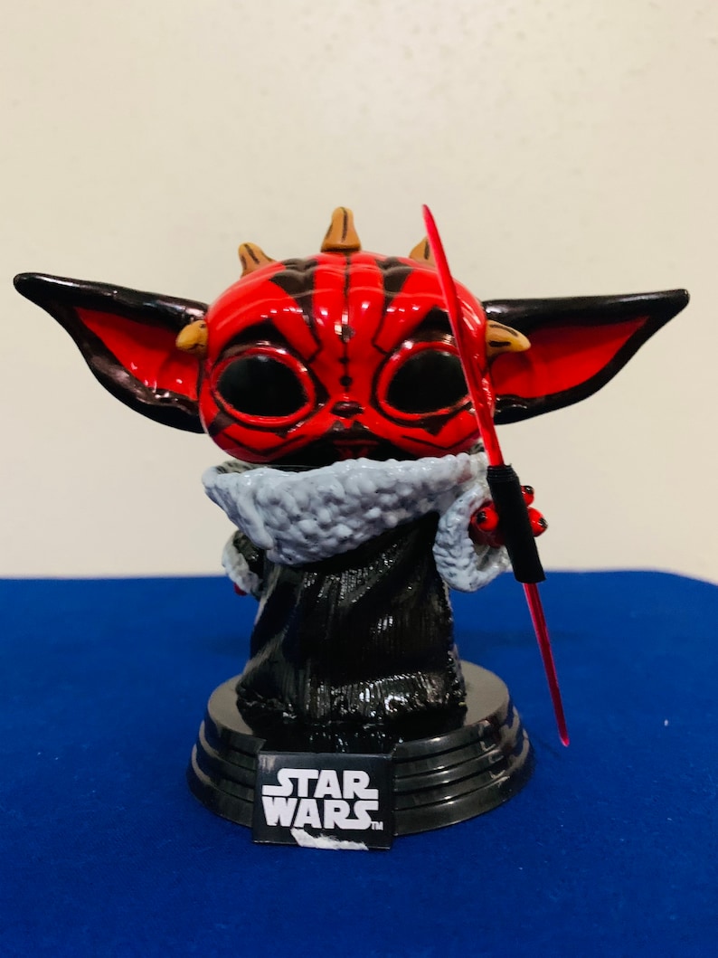 May include: A red and black Star Wars character figurine with horns and a lightsaber. The figurine is standing on a black base with the Star Wars logo.