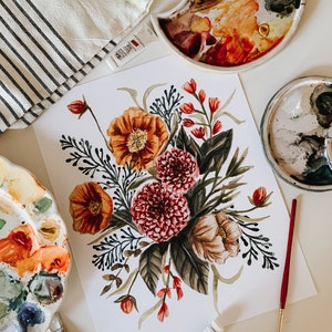 May include: A watercolour painting of a floral bouquet featuring red, orange, and green flowers. The painting is on white paper and is surrounded by paint palettes and paint tubes.