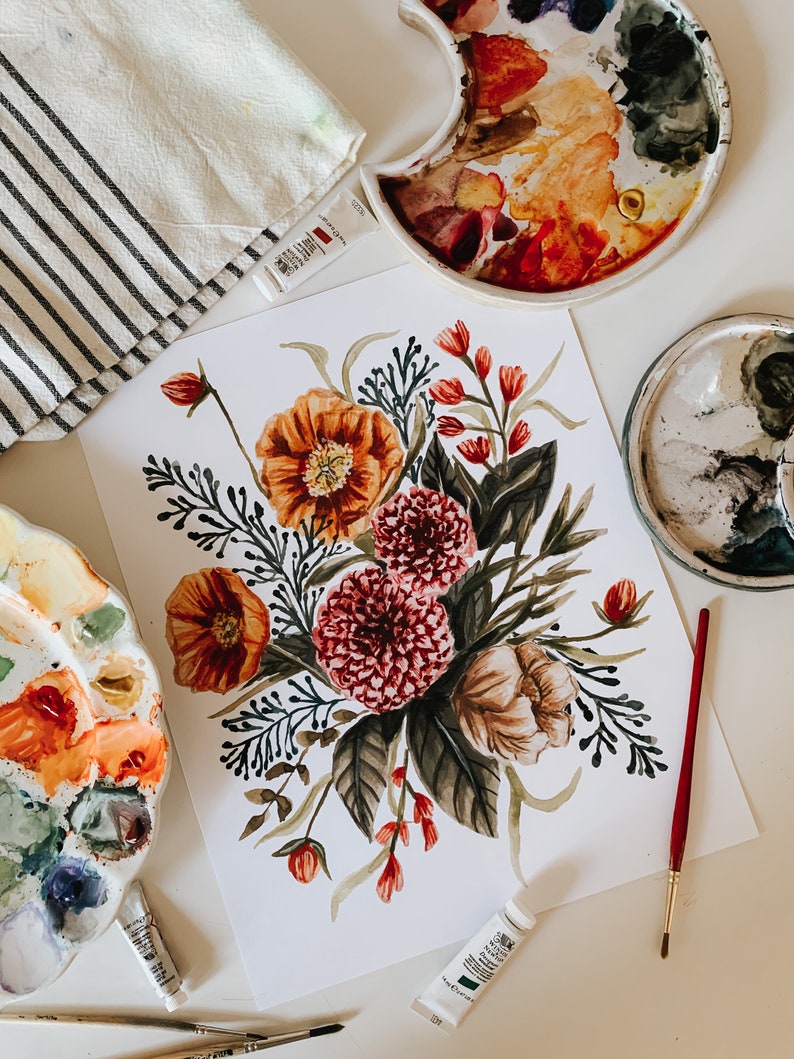 May include: A watercolour painting of a floral bouquet featuring red, orange, and green flowers. The painting is on white paper and is surrounded by paint palettes and paint tubes.