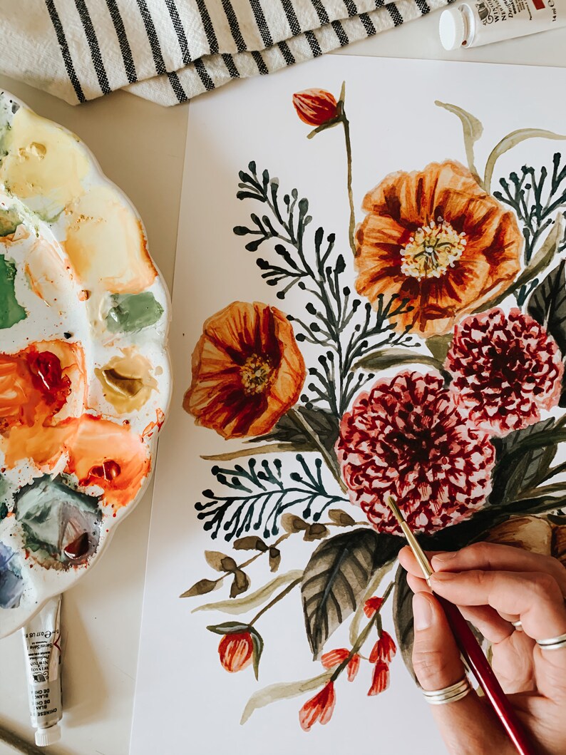 May include: A watercolour painting of a floral bouquet featuring red, orange, and green flowers. The painting is on a white background and is being painted by a person using a paintbrush.