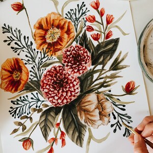 May include: Watercolour painting of a floral bouquet featuring orange, red, and brown flowers. The bouquet is painted on white paper and is being worked on by an artist.