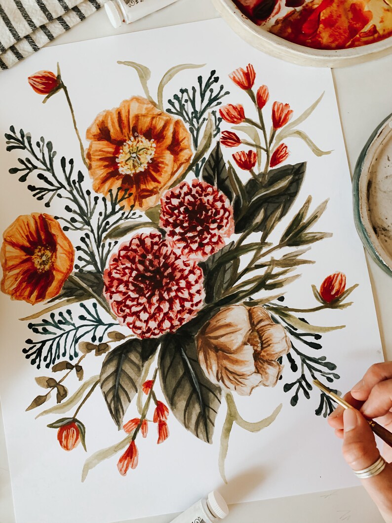 May include: Watercolour painting of a floral bouquet featuring orange, red, and brown flowers. The bouquet is painted on white paper and is being worked on by an artist.