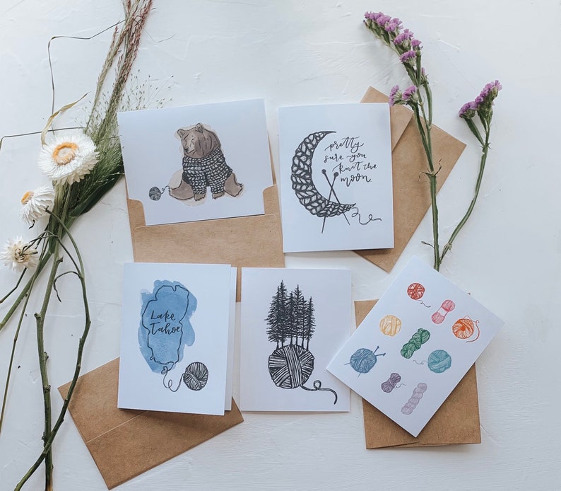May include: Set of five greeting cards with a nature theme. The cards feature illustrations of a bear knitting, a forest scene, a lake, a moon, and yarn balls. The cards are printed on white cardstock and have a brown envelope.