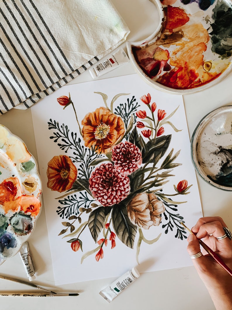 May include: A watercolour painting of a floral bouquet with orange, red, and white flowers. The flowers are surrounded by dark green leaves and stems. The painting is on a white background.