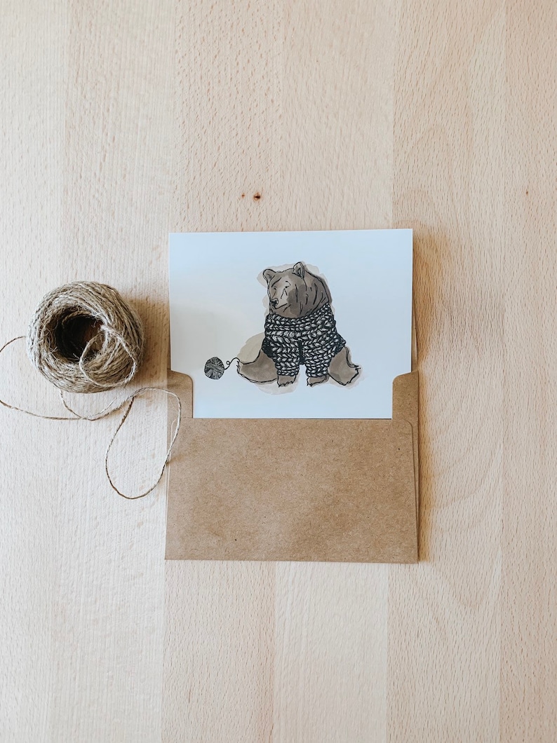 May include: A brown bear wearing a knitted sweater sits with a ball of yarn. The bear is drawn in a cartoon style with a simple background.