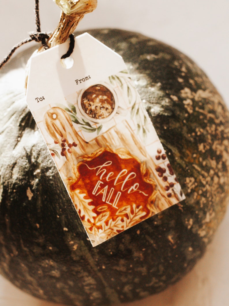 May include: A white gift tag with a watercolor illustration of fall leaves, a pie, and a cup of coffee. The tag says "hello fall" and has spaces for "to" and "from".