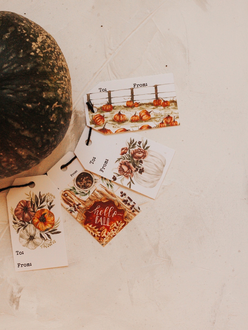 May include: Four gift tags with fall-themed designs. The tags are white with black text that says "To:" and "From:". The designs include pumpkins, a white pumpkin with flowers, and a wooden sign with the text "hello fall".