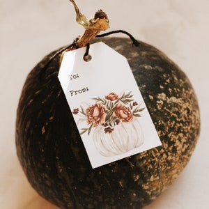 May include: A green gourd with a brown stem and a white gift tag attached. The tag has a watercolor illustration of a white pumpkin with pink and orange flowers and the words "To:" and "From:" printed on it.