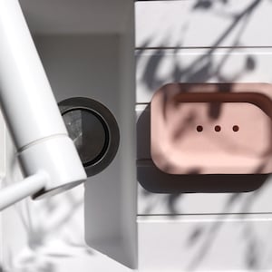 Könnte beinhalten: Eine hellrosa Seifenablage mit drei Abflusslöchern auf einer weißen Arbeitsplatte. Die Ablage ist aus glattem, mattem Material.