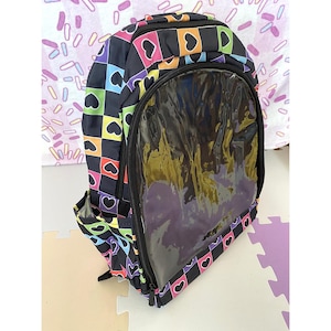 May include: A backpack featuring a black, checkered pattern with colorful hearts in shades of pink, orange, yellow, green, blue, and purple. The front includes a large, clear, transparent vinyl window pocket with a black zipper closure.