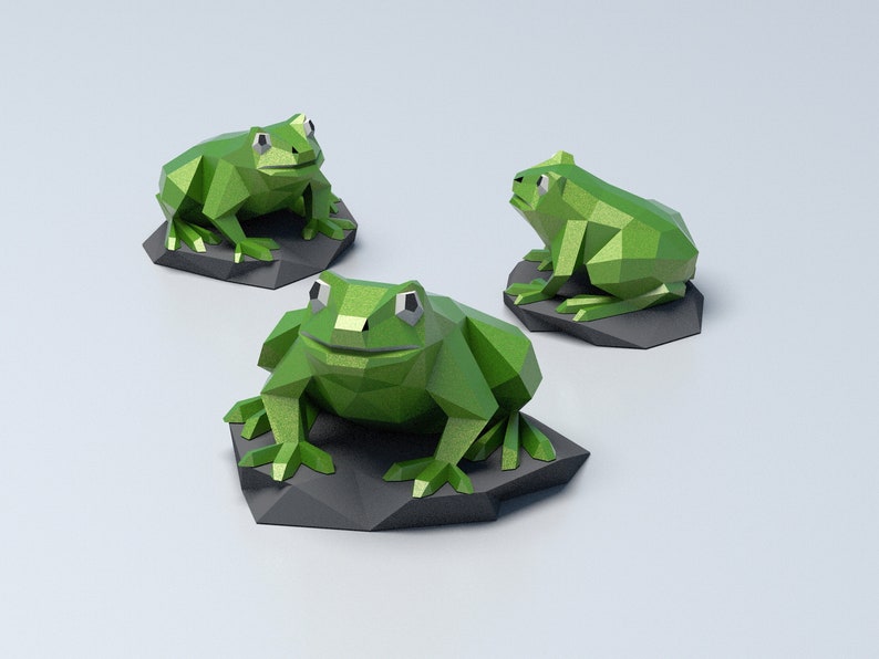 May include: Three origami frogs made of green paper, each sitting on a gray rock base. The frogs are in different poses, with one facing forward, one facing to the right, and one facing to the left.