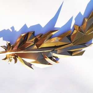 May include: A gold-colored, geometric feather sculpture with a sharp, pointed tip. The sculpture is made of many small, triangular pieces of metal that are joined together to create a three-dimensional effect.