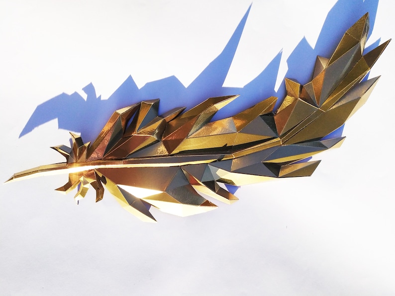 May include: A gold-colored, geometric feather sculpture with a sharp, pointed tip. The sculpture is made of many small, triangular pieces of metal that are joined together to create a three-dimensional effect.